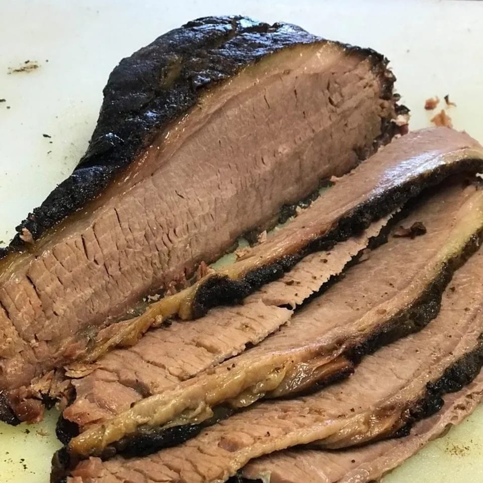 Close-up of a large, juicy, sliced brisket with a dark, smoky bark on a cutting board.