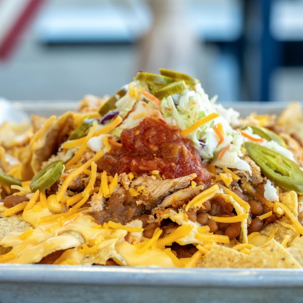 Close-up of loaded nachos with shredded chicken, beans, cheese, salsa, coleslaw, and jalapeños.