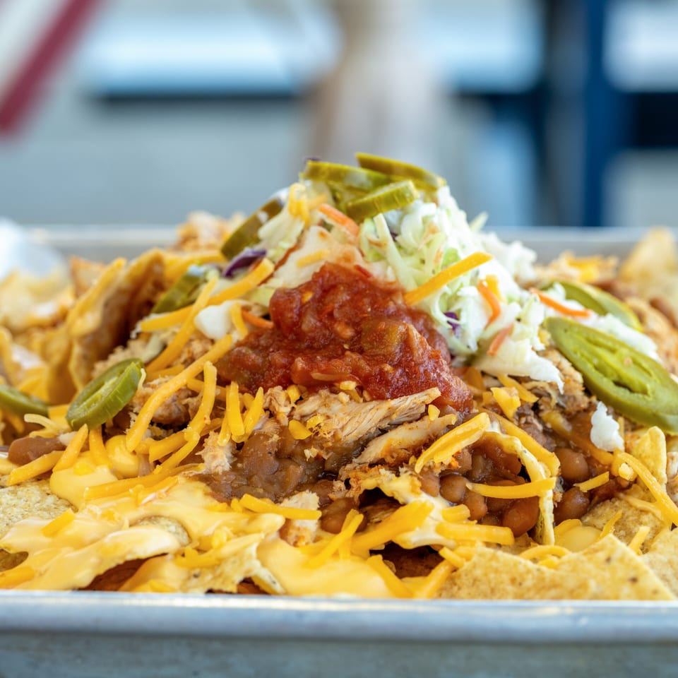 Close-up of loaded nachos with shredded chicken, beans, cheese, salsa, coleslaw, and jalapeños.