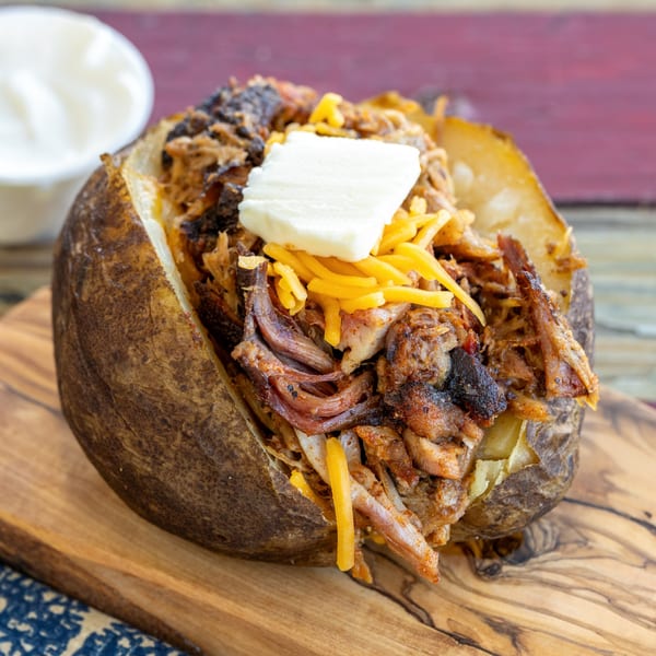 Baked potato loaded with pulled pork, shredded cheddar cheese, and a pat of butter.