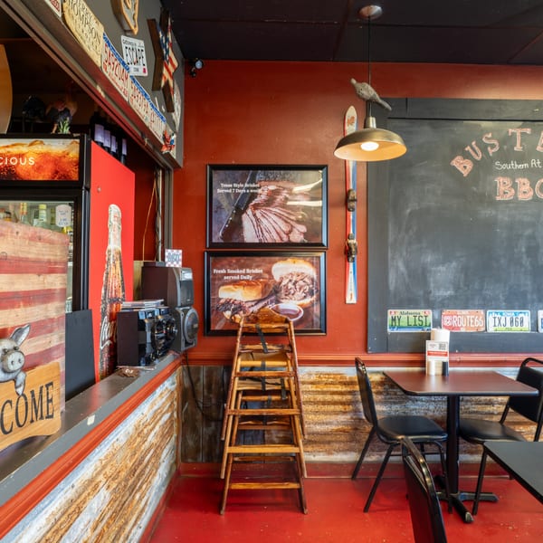 Interior of a rustic BBQ restaurant with red walls, chalkboard menu, and brisket advertisements.
