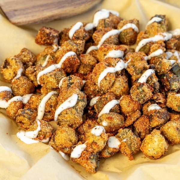 Crispy fried mushrooms, seasoned with spices and drizzled with a creamy white sauce, served on parchment paper.