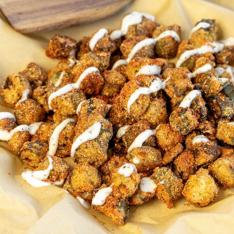 Crispy fried mushrooms, seasoned with spices and drizzled with a creamy white sauce, served on parchment paper.