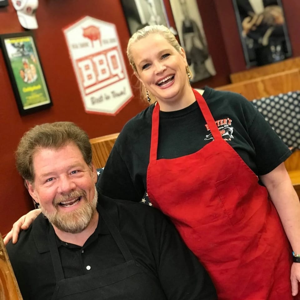 Two smiling Busters Southern Pit BBQ employees, a man and a woman in aprons, pose together.