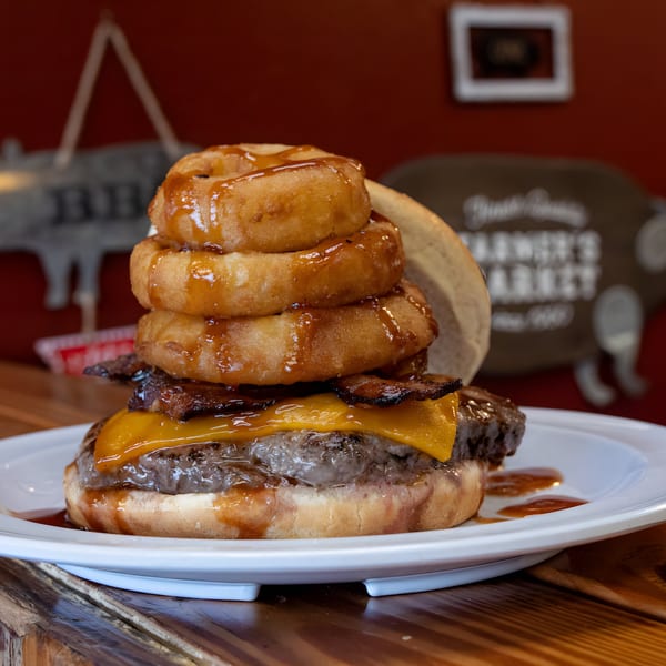 A Busters Southern Pit BBQ burger with cheese, bacon, and onion rings drizzled with sauce.