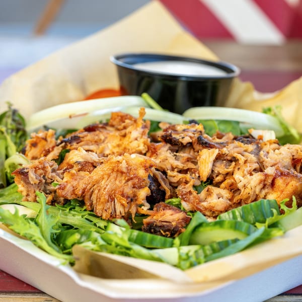 Pulled pork salad with mixed greens, cucumbers, onions, and a side of dressing in a takeout container.