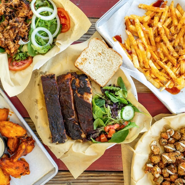 A feast of barbecue ribs, pulled pork salad, fries, chicken wings, and fried mushrooms on a rustic table.