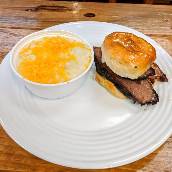 Busters Southern Pit BBQ brisket biscuit with a side of cheesy grits on a white plate.