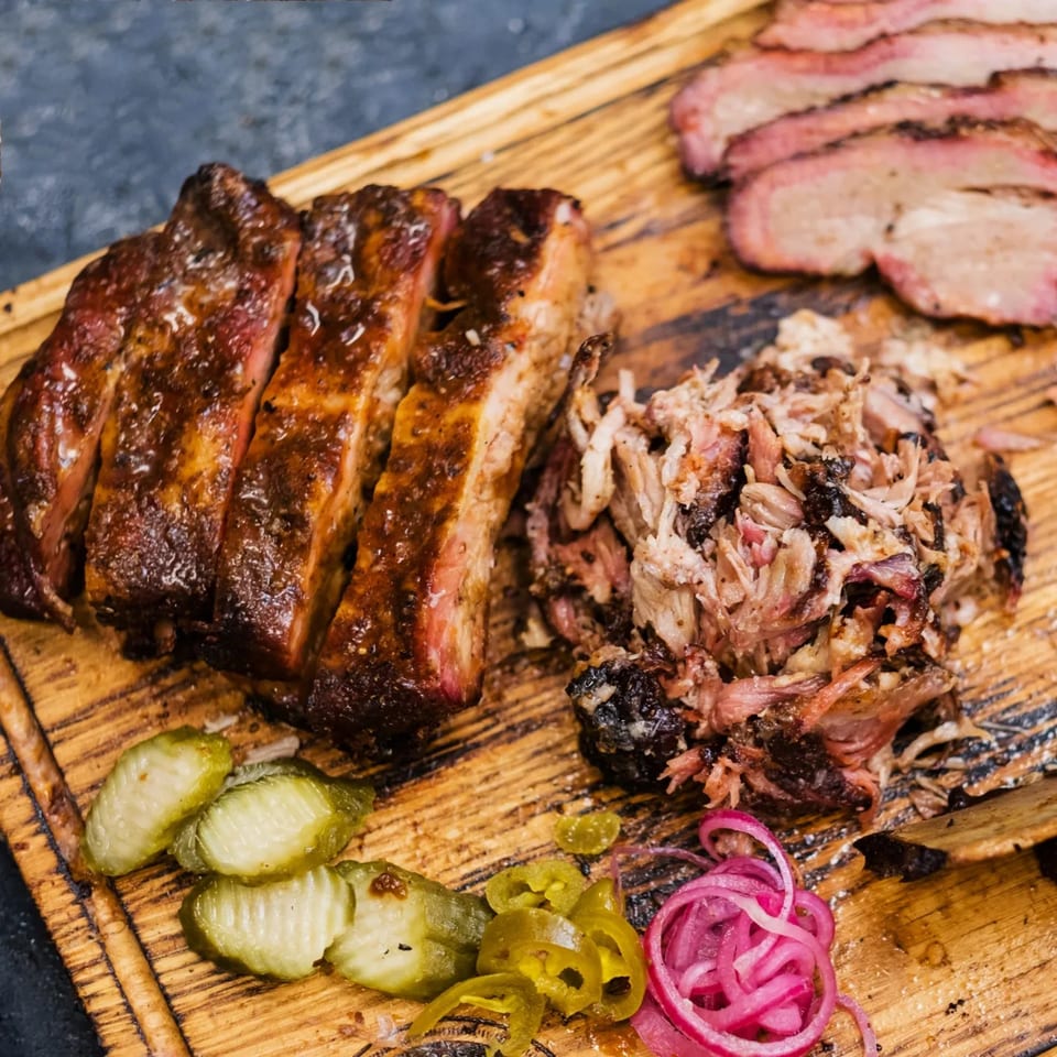 Buster's Southern Pit BBQ platter with ribs, pulled pork, brisket, pickles, and pickled onions.