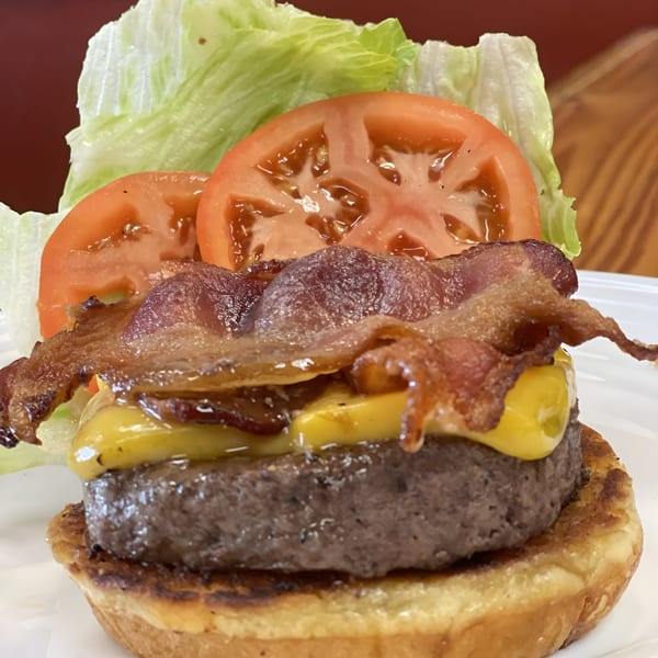 A Busters Southern Pit BBQ bacon cheeseburger with lettuce and tomato on a white plate.