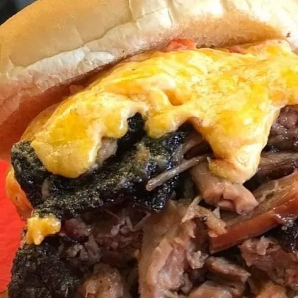 Close-up of a Busters Southern Pit BBQ sandwich with pulled pork, burnt ends, and melted cheese.