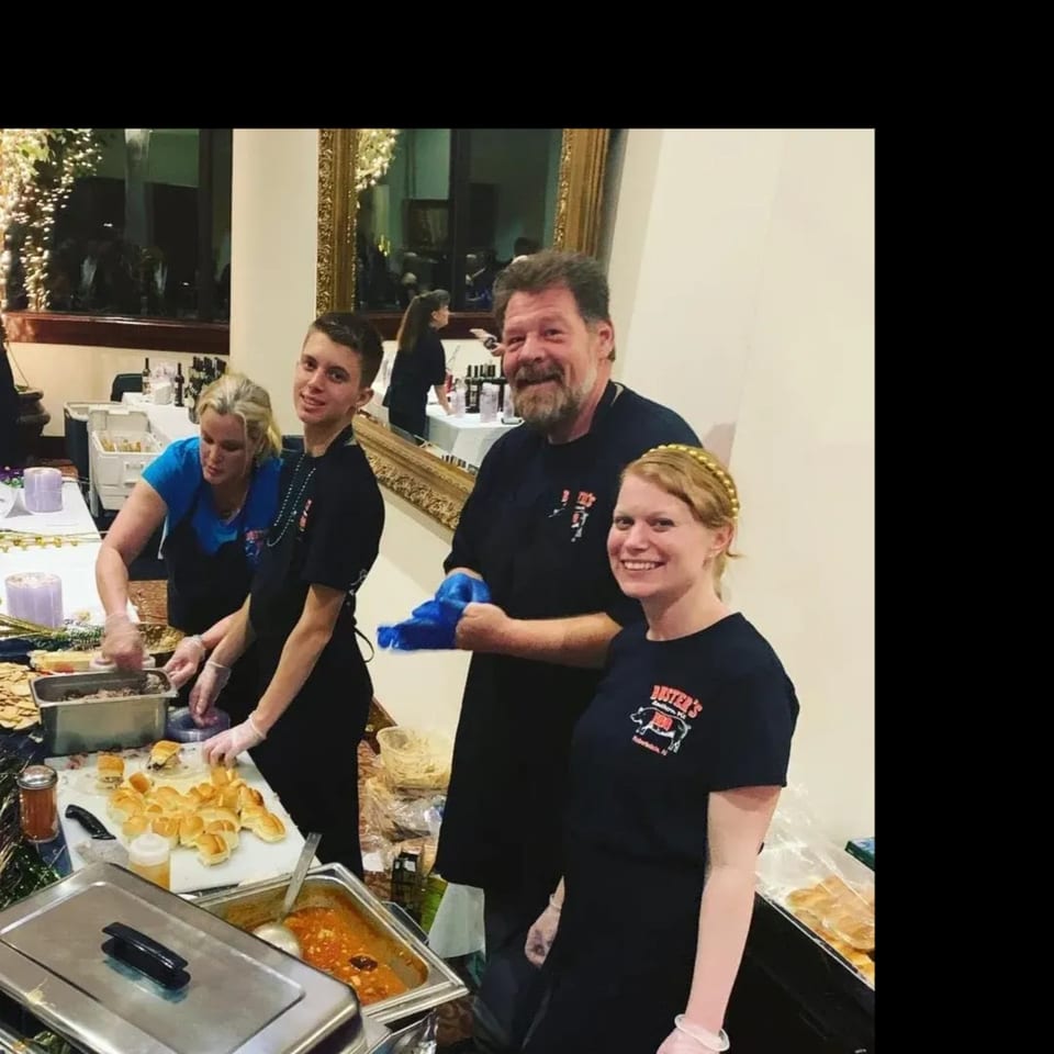 Busters Southern Pit BBQ staff serving food at a buffet, smiling at the camera.