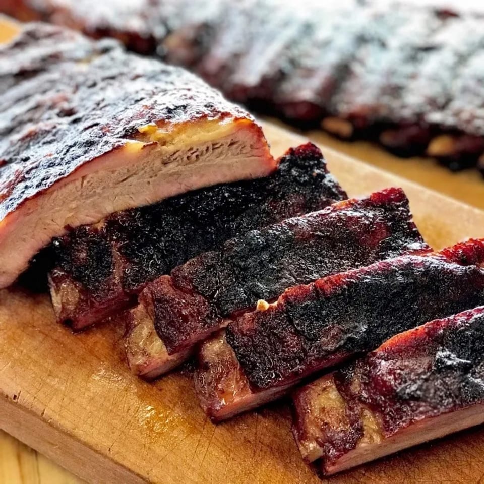 Close-up of a rack of Busters Southern Pit BBQ ribs, partially sliced on a wooden board.