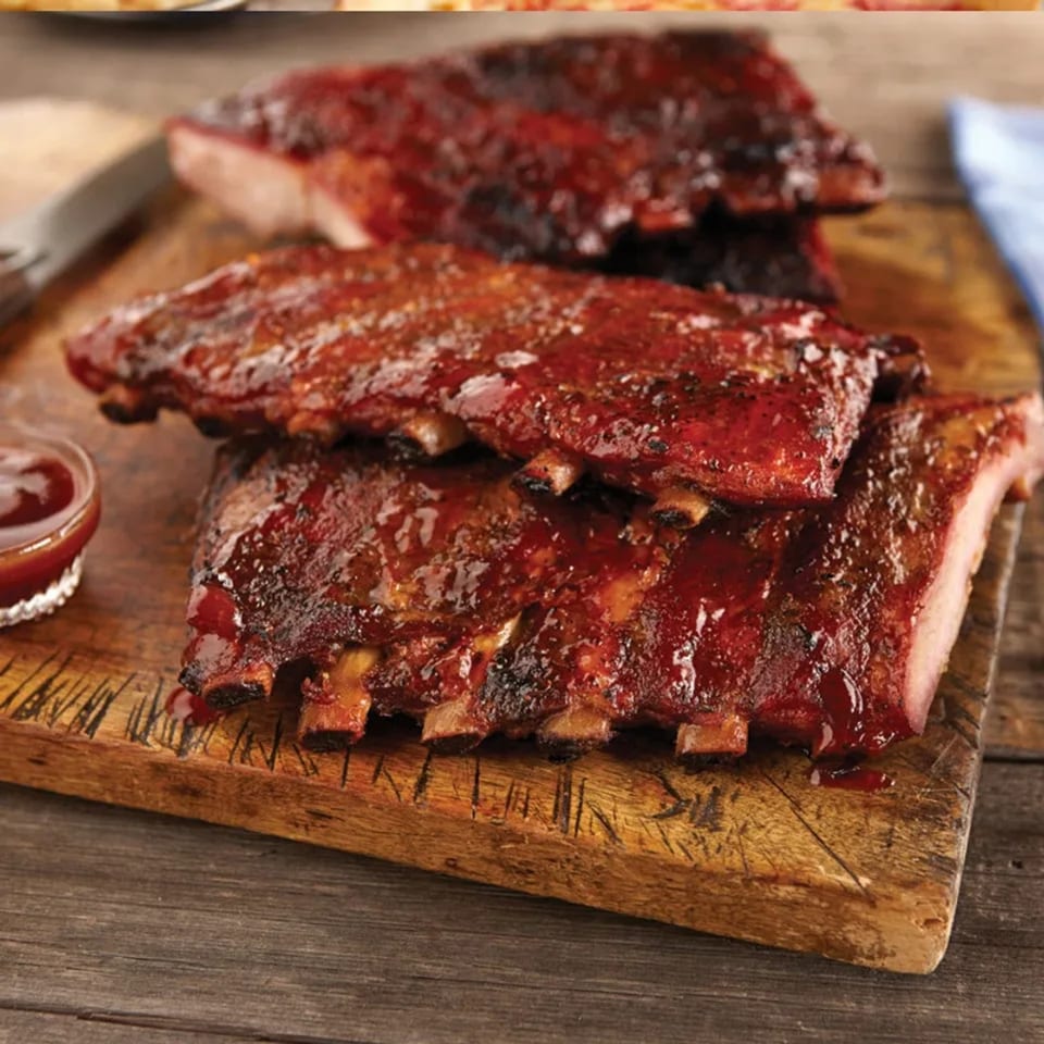 Three racks of Busters Southern Pit BBQ ribs, glistening with sauce, on a rustic wooden cutting board.