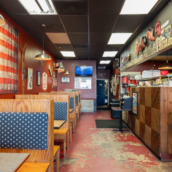 Interior of a casual restaurant with American flag decor, wooden booths, and a service counter.