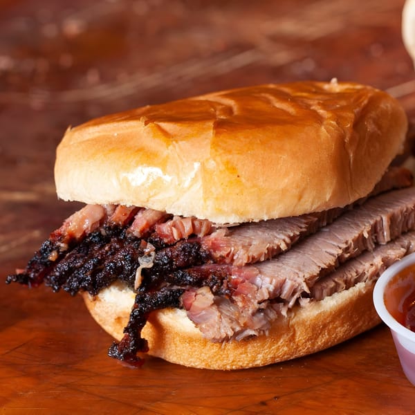 Close-up of a Busters Southern Pit BBQ brisket sandwich with a side of sauce.