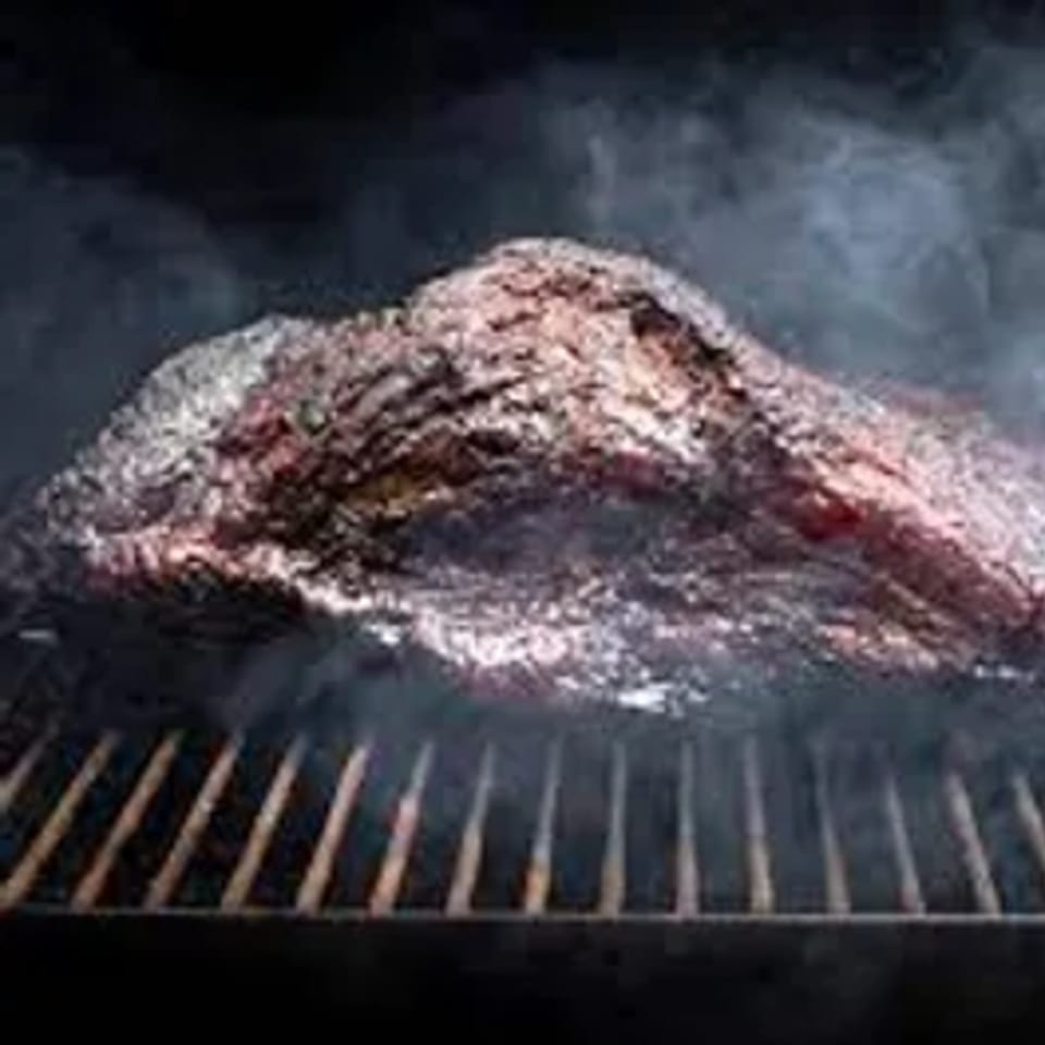A large cut of Busters Southern Pit BBQ brisket smoking on a grill.