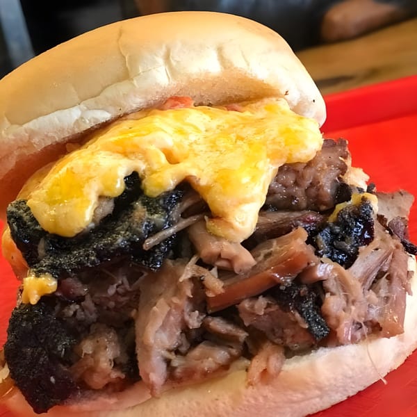 Close-up of a Busters Southern Pit BBQ sandwich with pulled pork, burnt ends, and melted cheese.